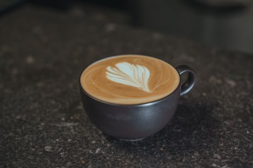 Free Close-up of a latte with intricate foam art on a dark countertop, capturing the essence of a cozy café experience. Stock Photo