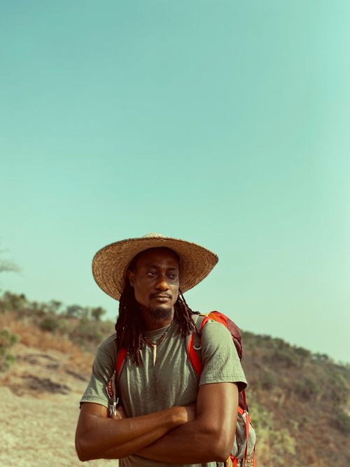 Free Man with straw hat on a sunny day, hiking with a backpack through a scenic trail. Stock Photo