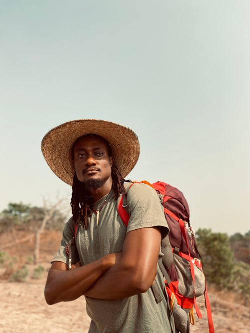 Free Man in a straw hat posing with a backpack outdoors on a sunny day. Stock Photo
