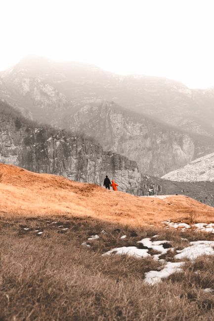 Two people stroll through a foggy, mountainous landscape during winter.