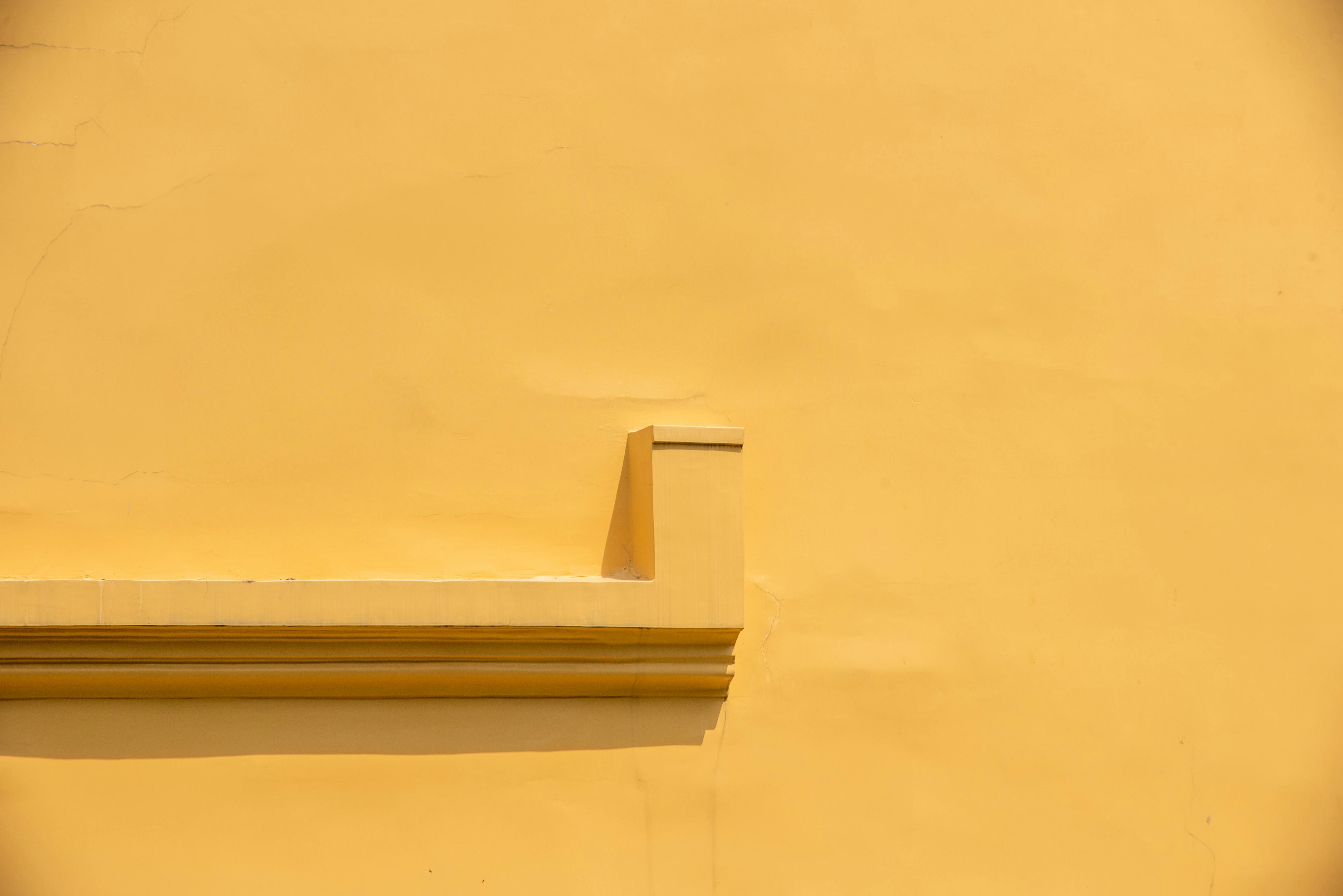 Gratis Abstrakt visning af en minimalistisk gul stukvæg med arkitektoniske detaljer, der giver en beroligende baggrund. Lagerfoto