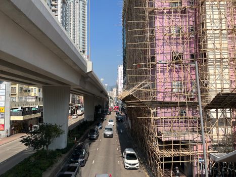 Dynamic street scene in Kowloon, Hong Kong, highlighting bamboo scaffolding and modern urban architecture.