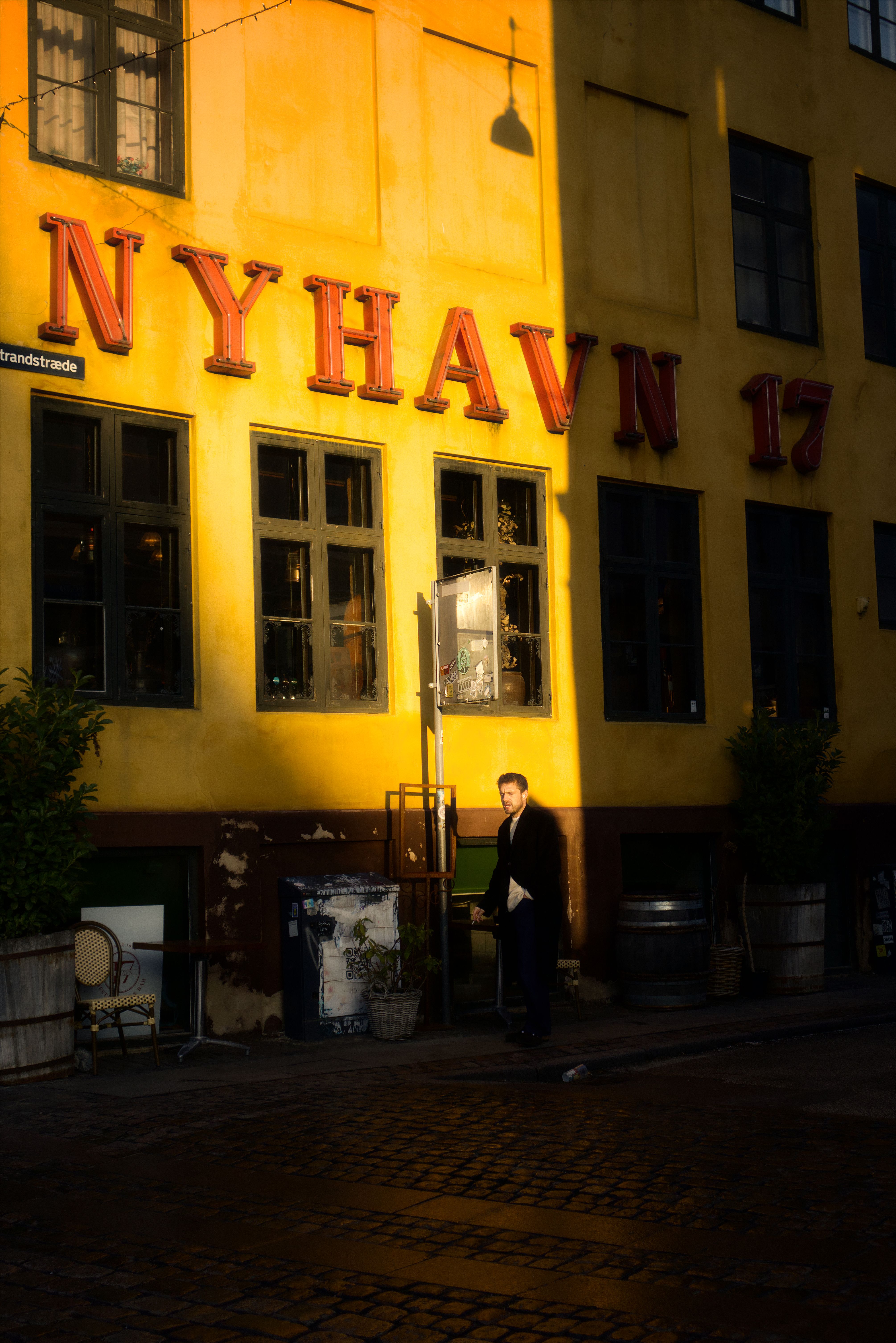 Man walking by Nyhavn 17 in Copenhagen during sunset, showcasing urban street life.