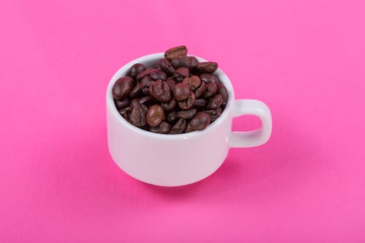 A cup filled with roasted coffee beans on a vibrant pink backdrop, perfect for a coffee-themed design.