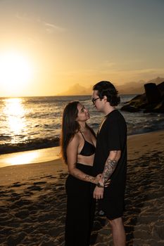 Couple embracing on a Rio de Janeiro beach at sunset, capturing a romantic moment by the ocean.