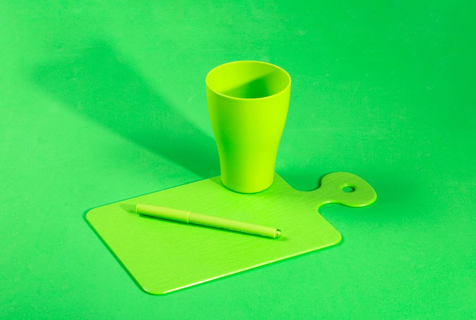 An artistic display of a lime green cup, pen, and cutting board on a matching background.