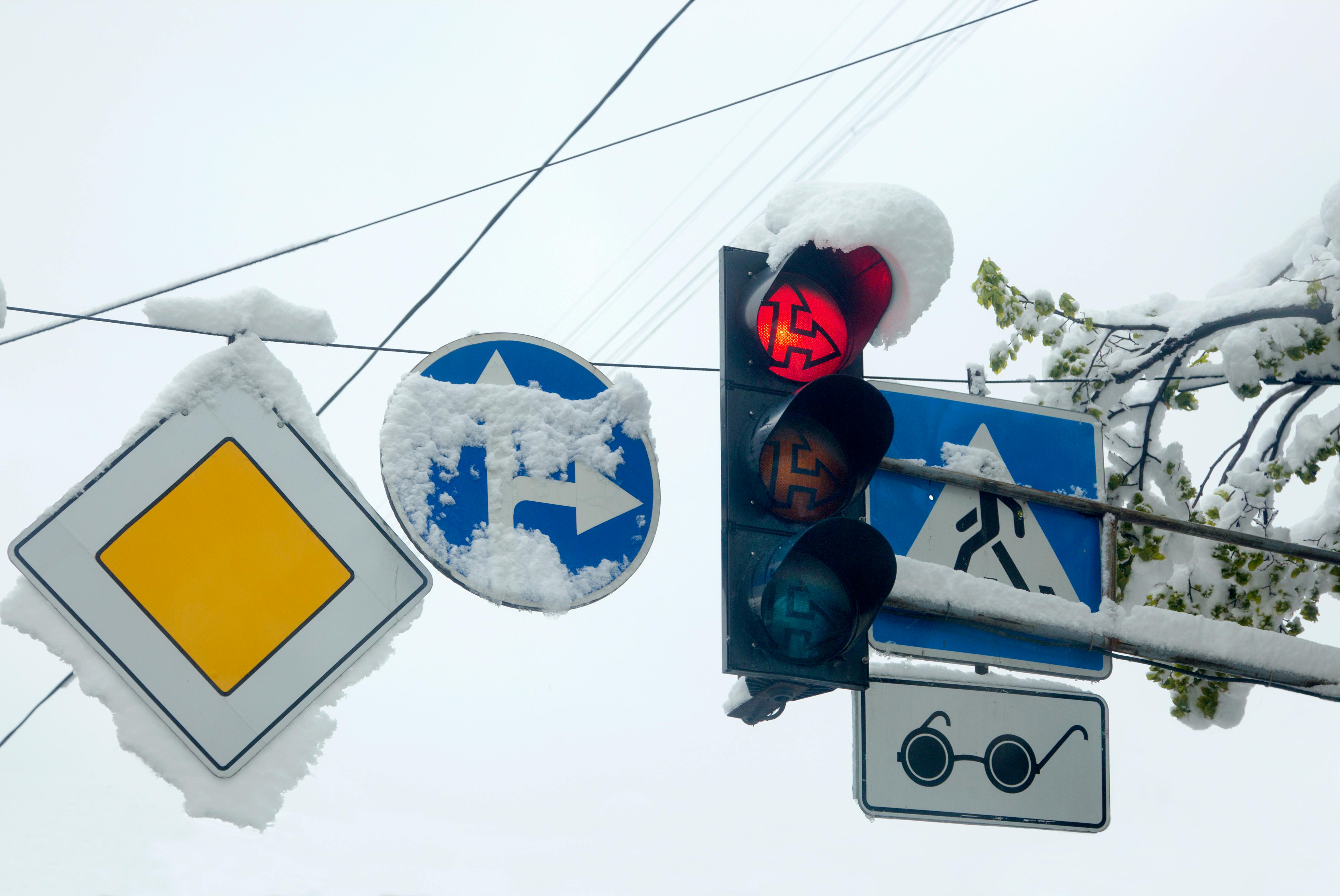 Snow-covered traffic light and signs, signaling a winter day with snowflakes.