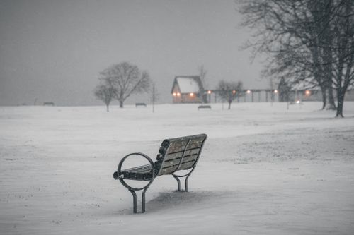 Free A solitary bench in a snowy park with a distant cozy cabin. Stock Photo