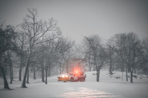 Free A snowplow truck with flashing lights clearing snow in a winter forest setting. Stock Photo
