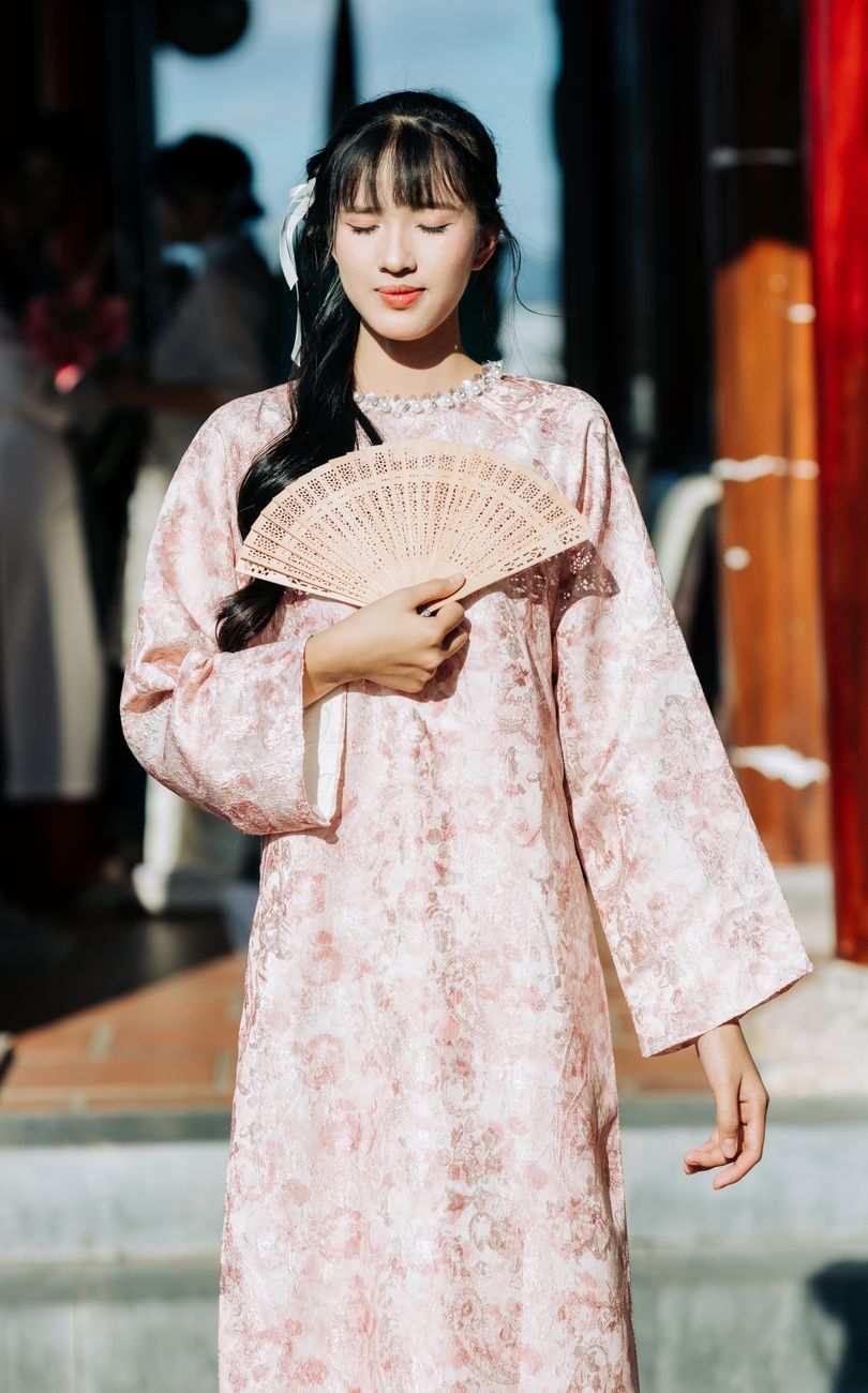 Vietnamese woman wearing Ao Dai in Kon Tum, Vietnam, holding a fan.