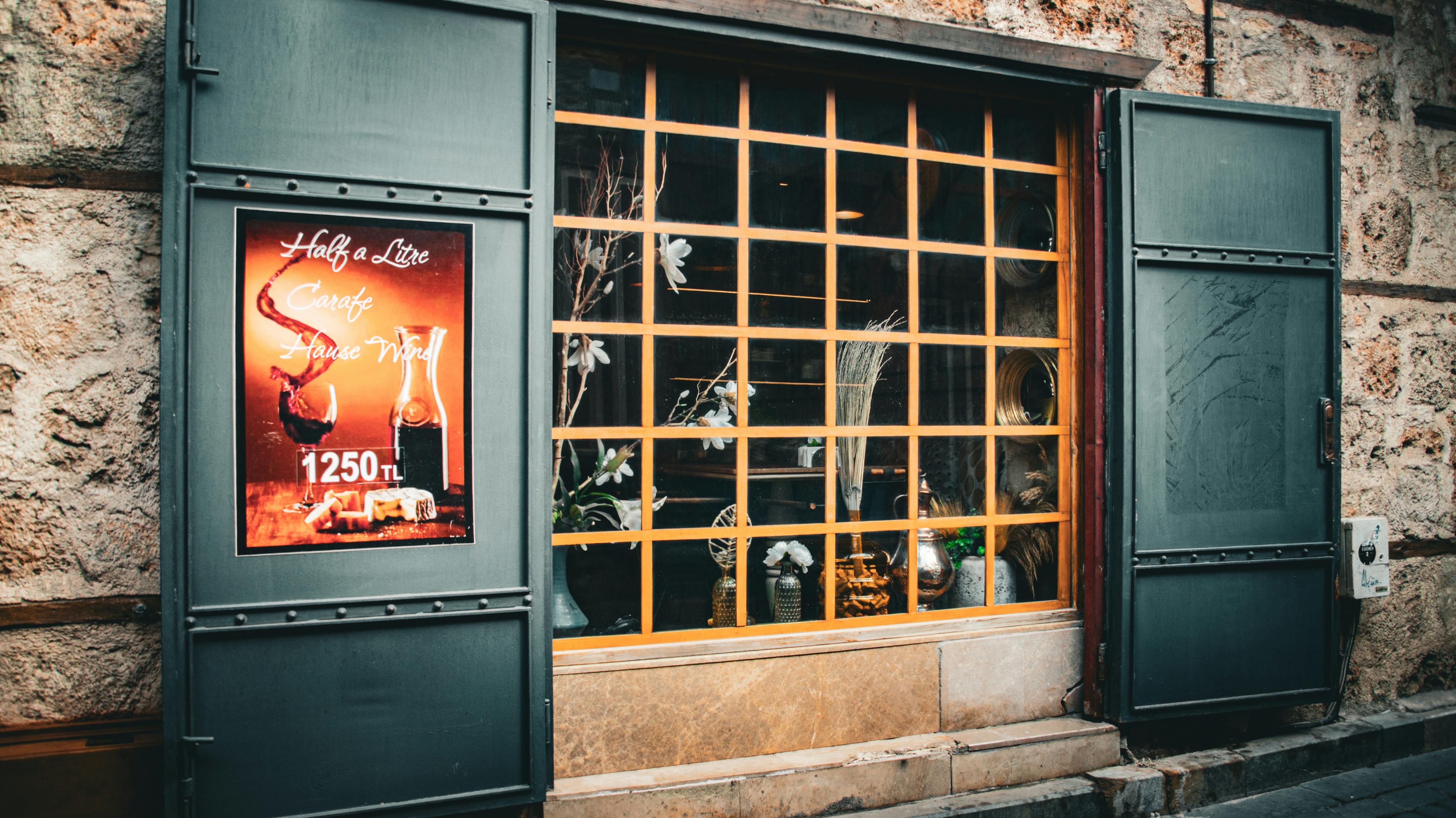 Ilmainen Viehättävä näkymä ravintolan ikkunasta, jossa on viinijuliste ja maalaismainen sisustus. Kuvapankkikuva