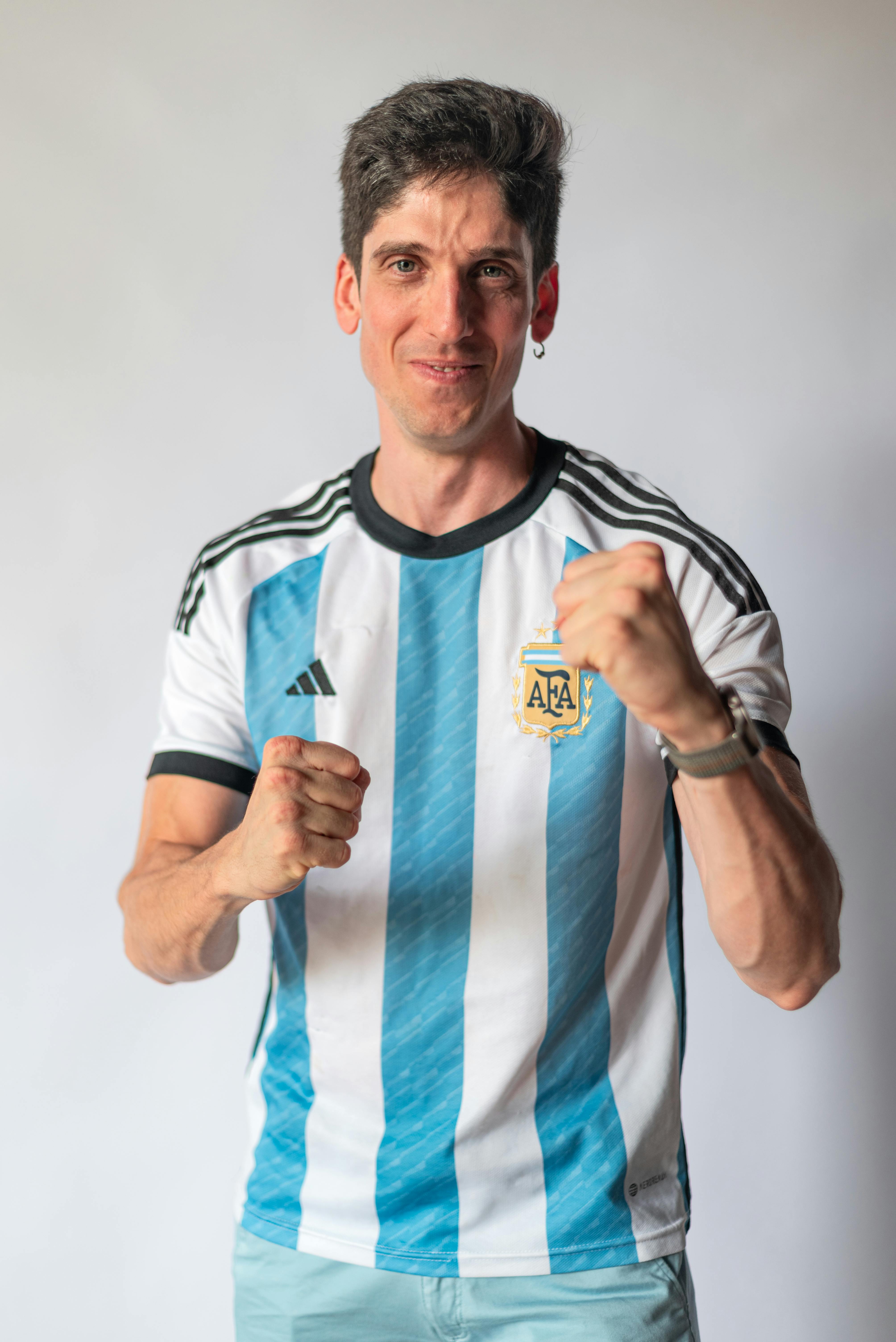 Excited Argentinian soccer fan cheering in team jersey with fists raised.