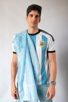 Portrait of a man in an Argentinian football jersey holding the national flag.