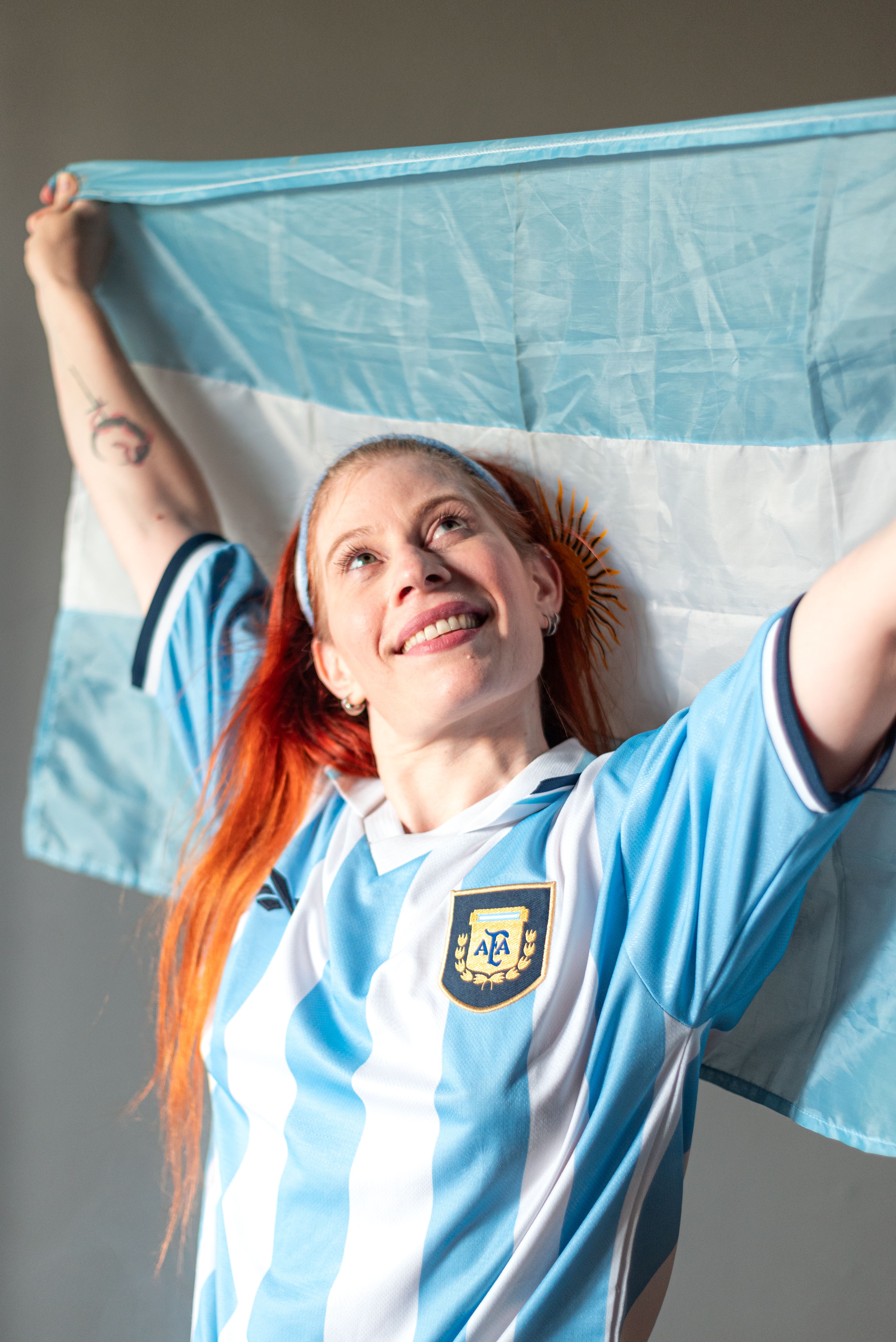 Smiling woman in Argentine jersey holding flag, celebrating victory.