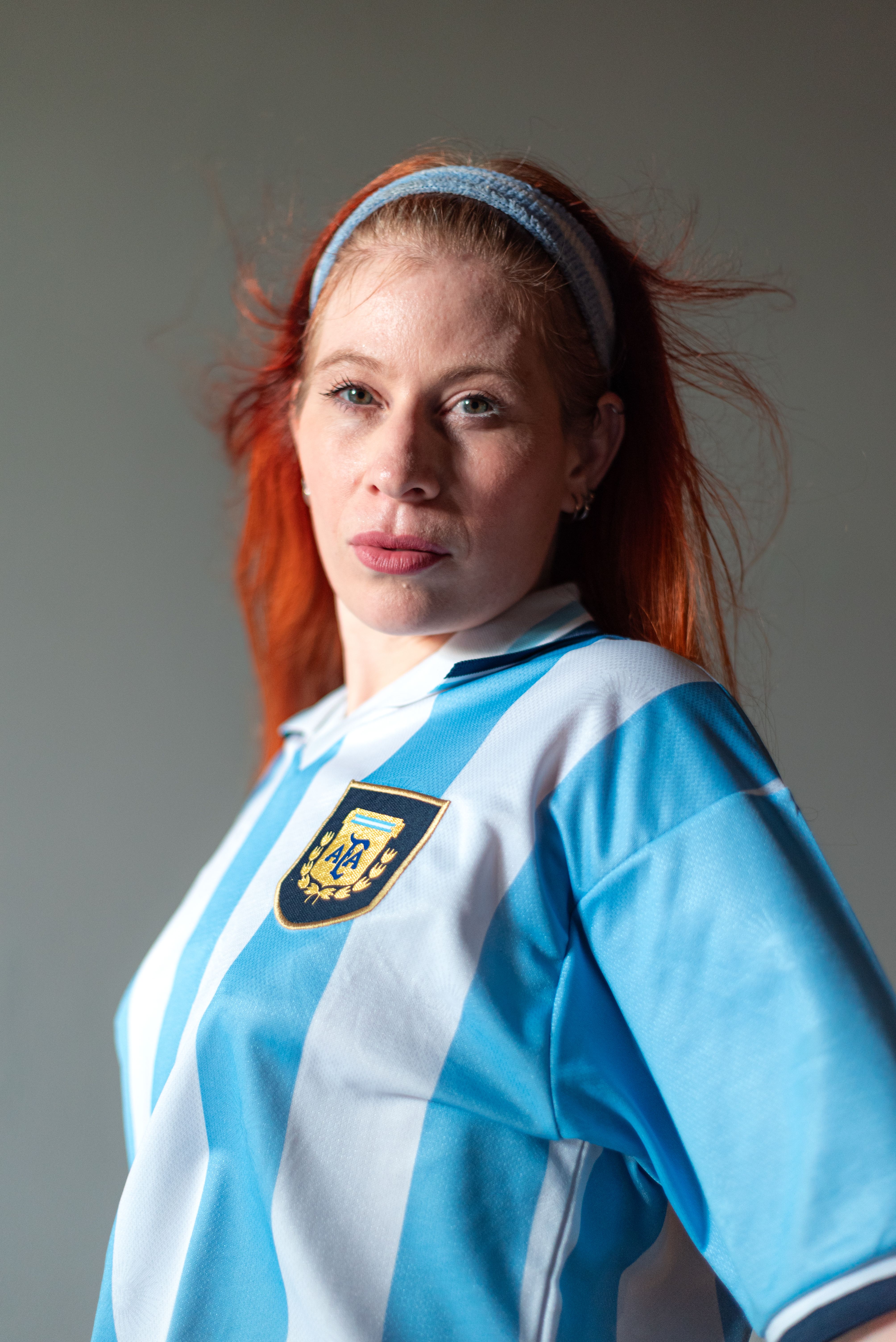 Confident woman posing in light wearing an Argentine football jersey.
