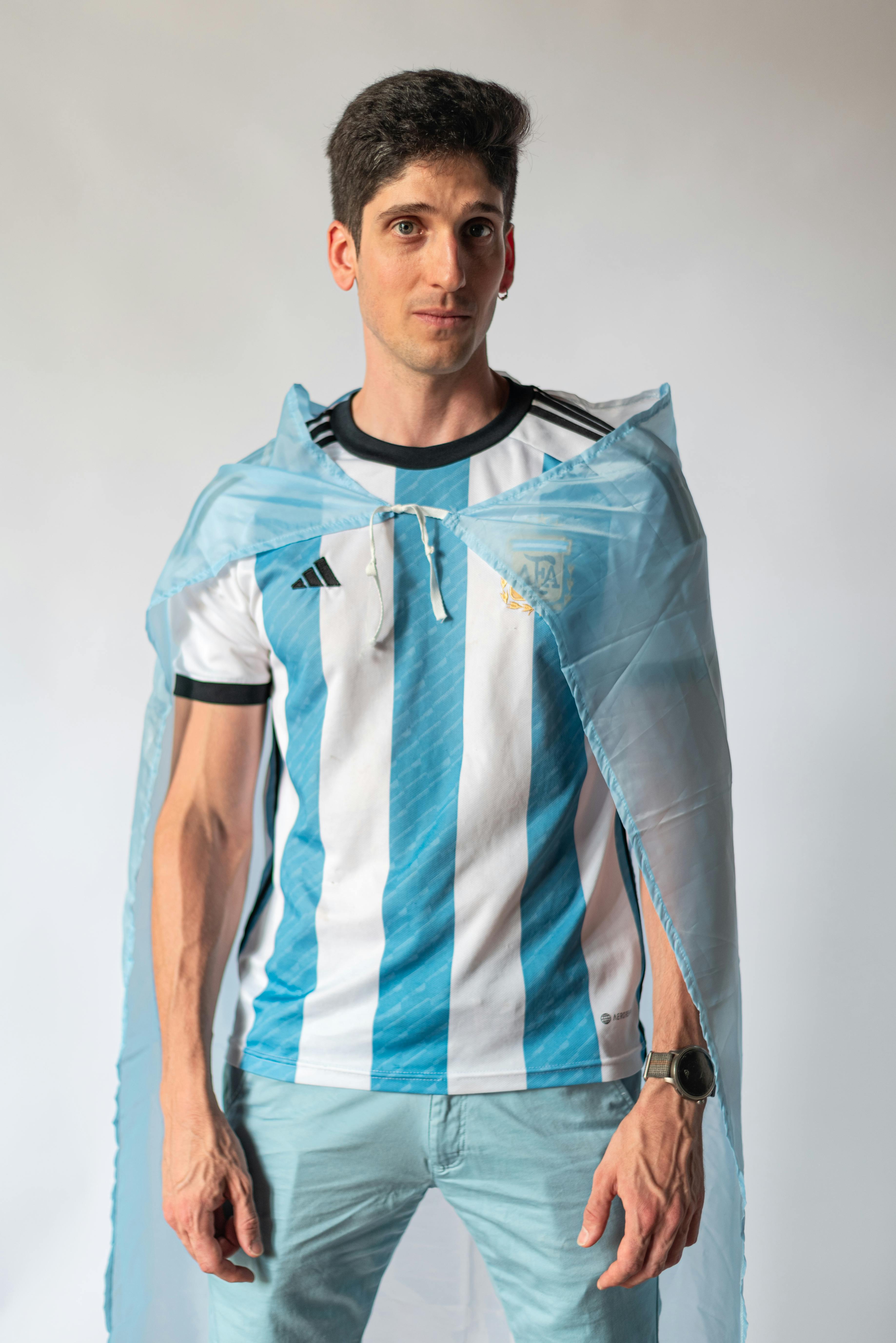 Man wearing Argentinian football shirt and cape, symbolizing national pride.