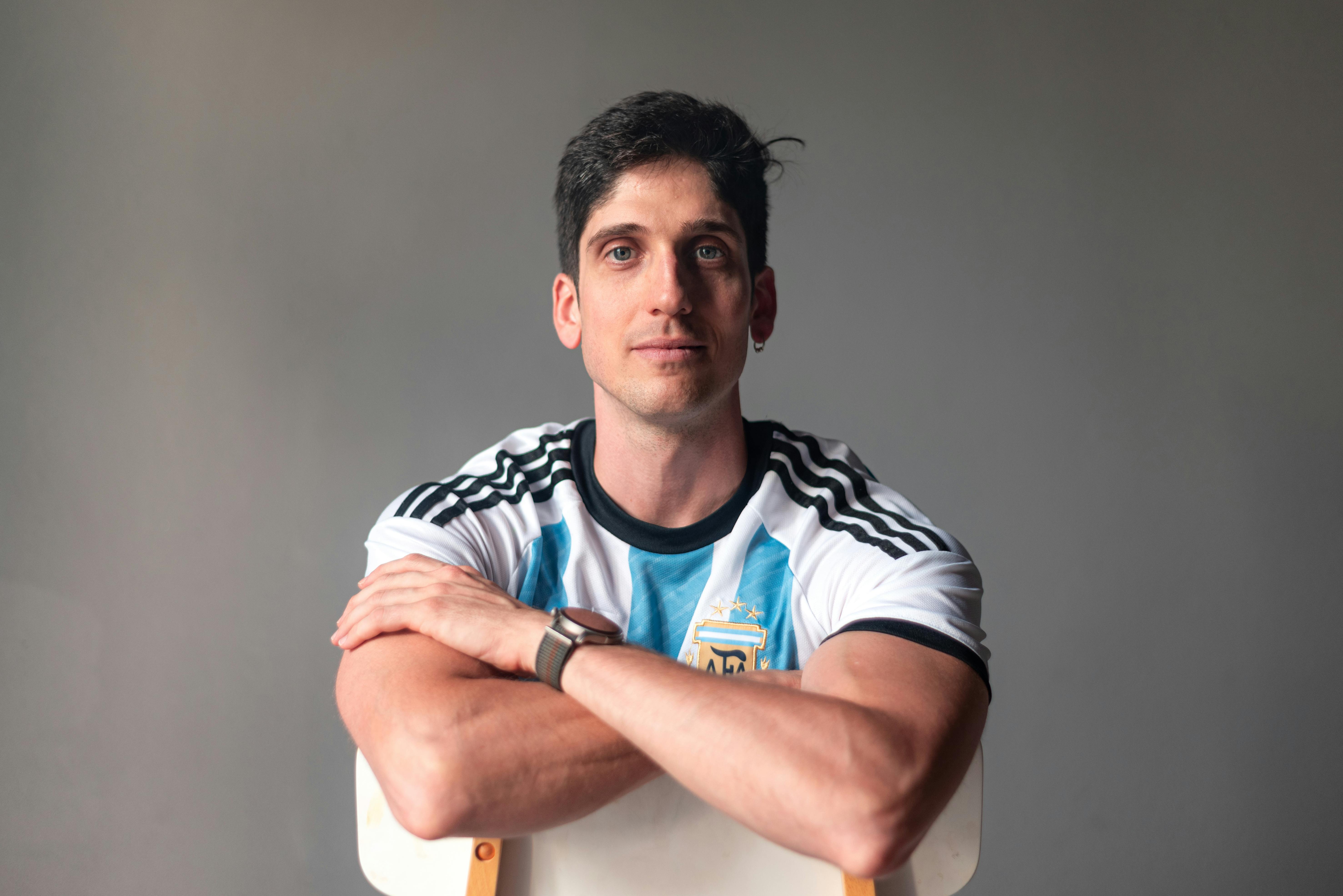 A confident man wearing the Argentine national football jersey, posing indoors.