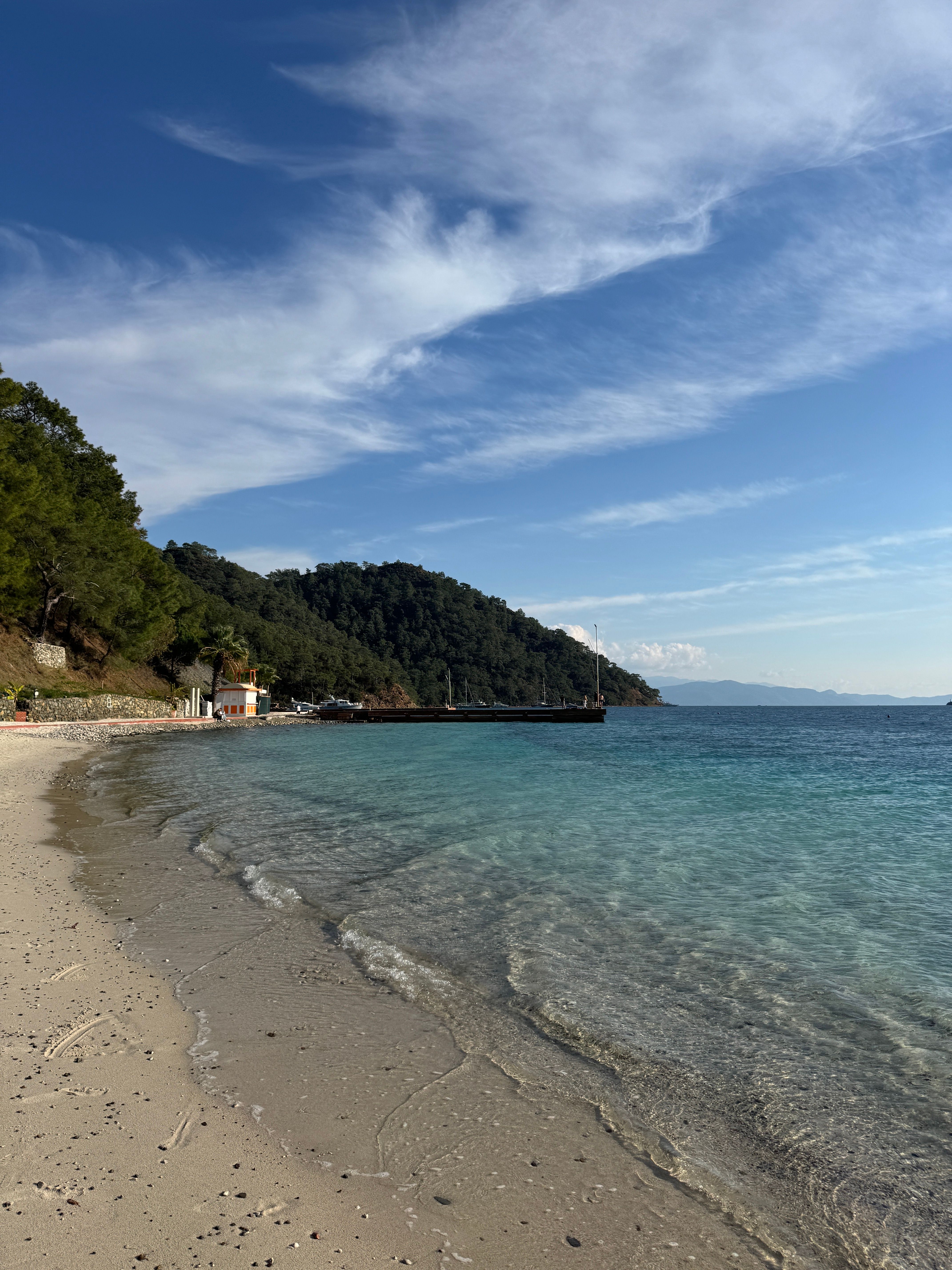 Scenic view of a serene beach with clear waters and a lush hillside under a bright sky.