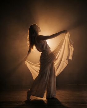 Silhouetted woman dancing gracefully in flowing dress, illuminated by warm backlight.