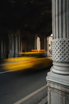 A motion-blurred yellow taxi rushes beneath a historic stone archway, capturing city life motion.