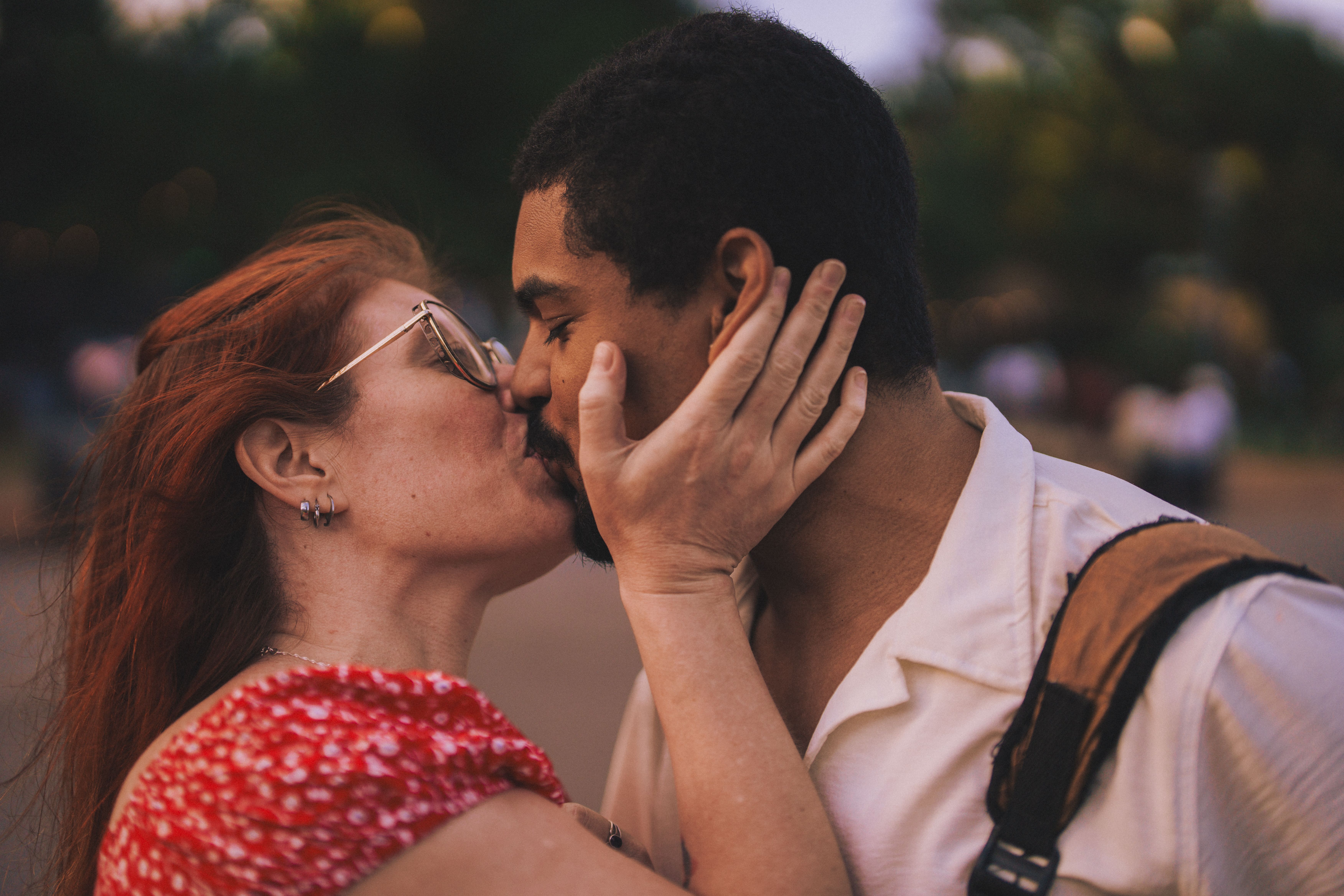 A couple sharing a slow, tender kiss outdoors, faces close in soft light.