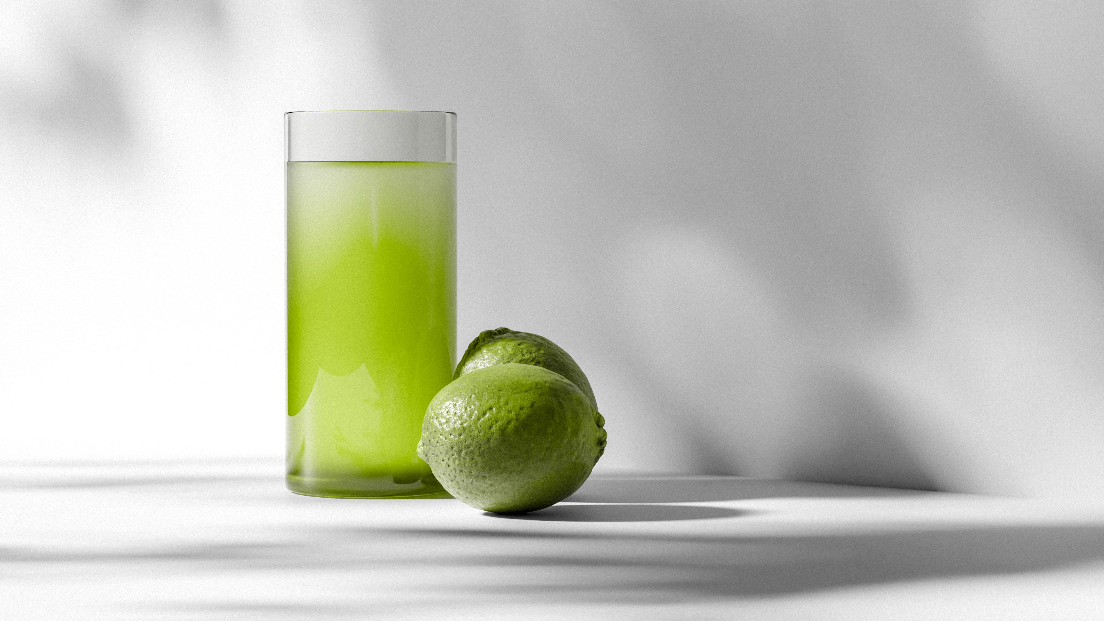 Fresh lime juice in a glass accompanied by two whole limes on a white surface.