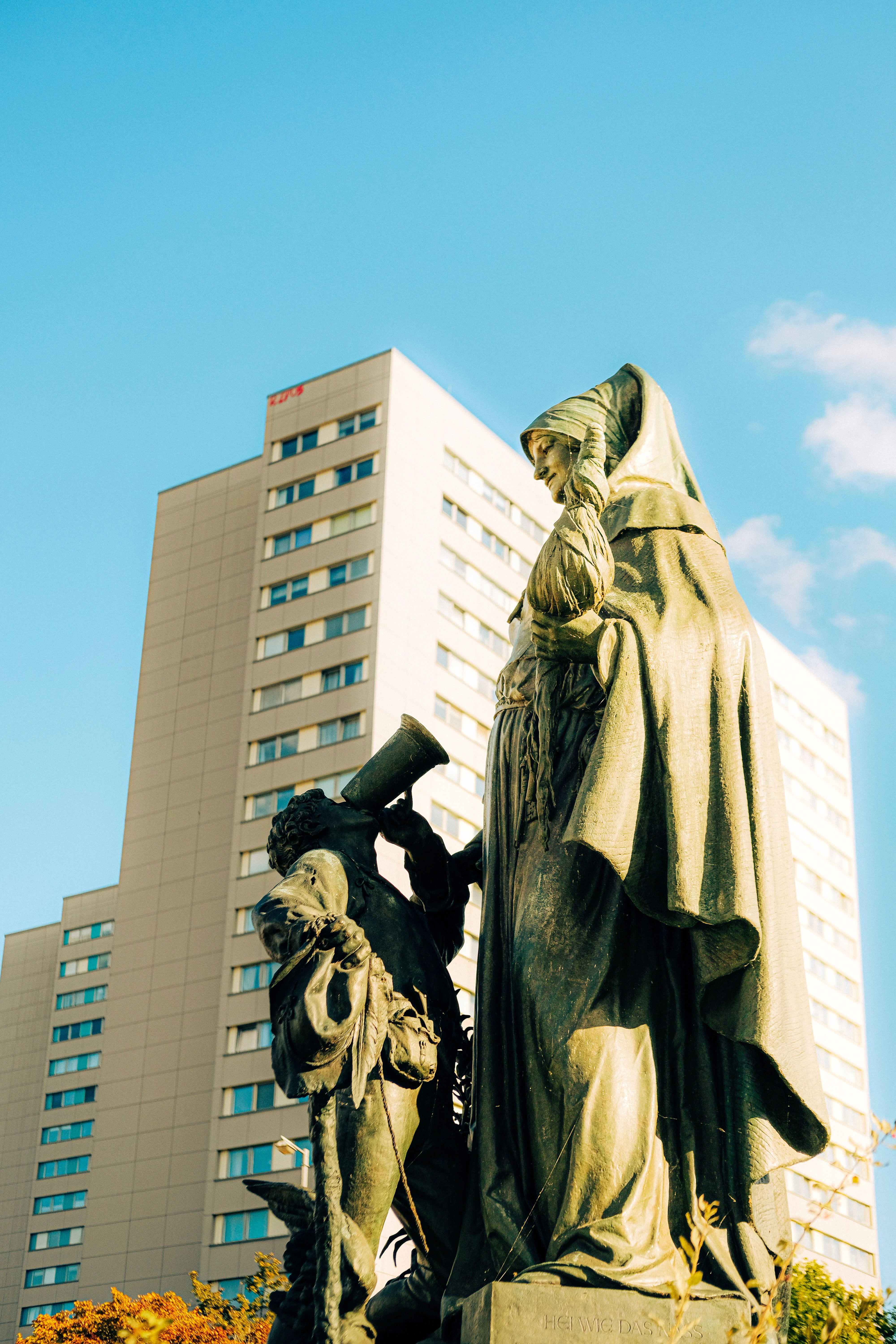 A majestic statue set against a modern building under a clear blue sky, blending history with urban life.