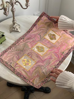 Decorative marbled paper with intricate Iznik tile patterns, held by a person.
