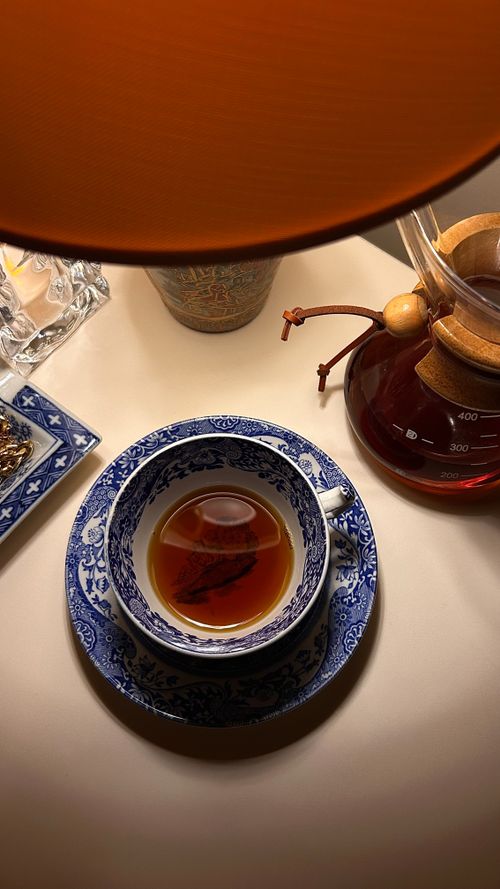 Free A cozy tea setting with a cup of tea in a blue porcelain cup under a warm lamp light. Stock Photo