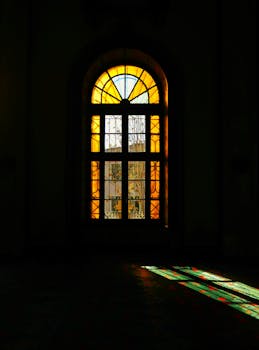 A dramatic view of a stained glass window casting colorful light in a dimly lit room.