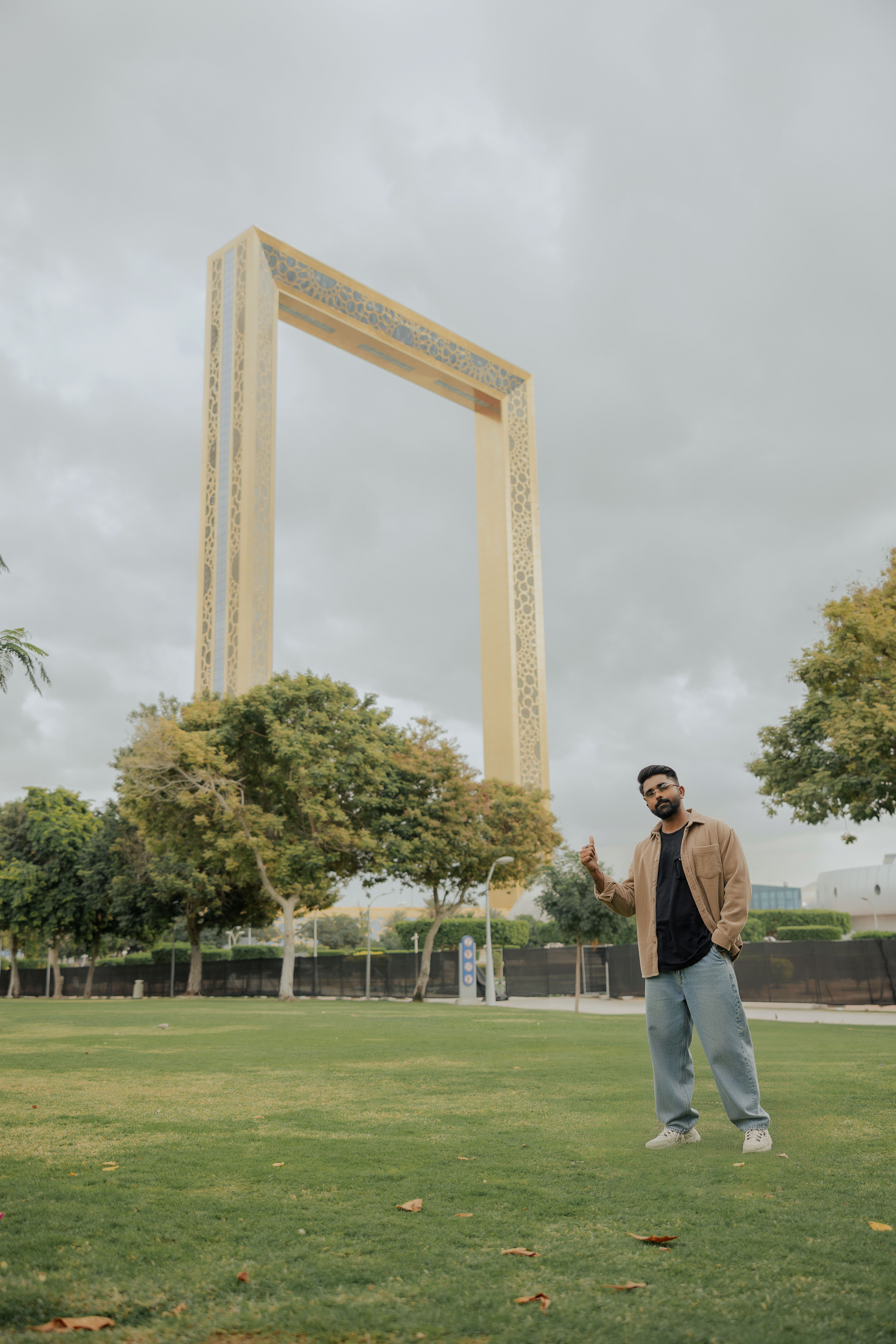A man poses in a park near the iconic Dubai Frame on a cloudy day.