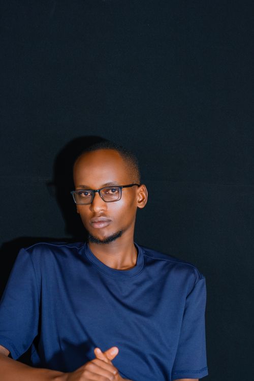 Free Portrait of a young man wearing glasses against a dark backdrop. Captured indoors. Stock Photo