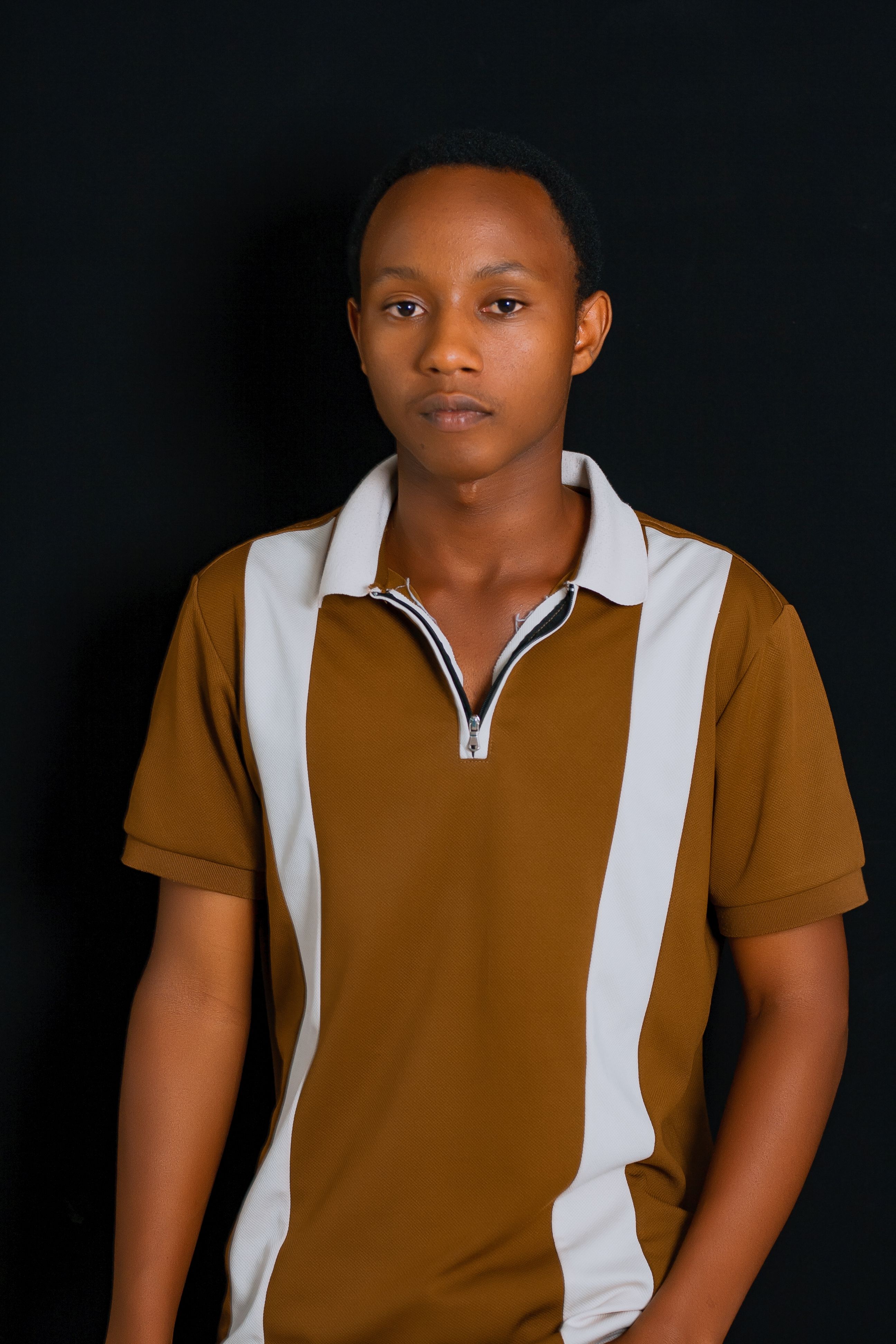 Young African adult posing against a black background, wearing a brown shirt.