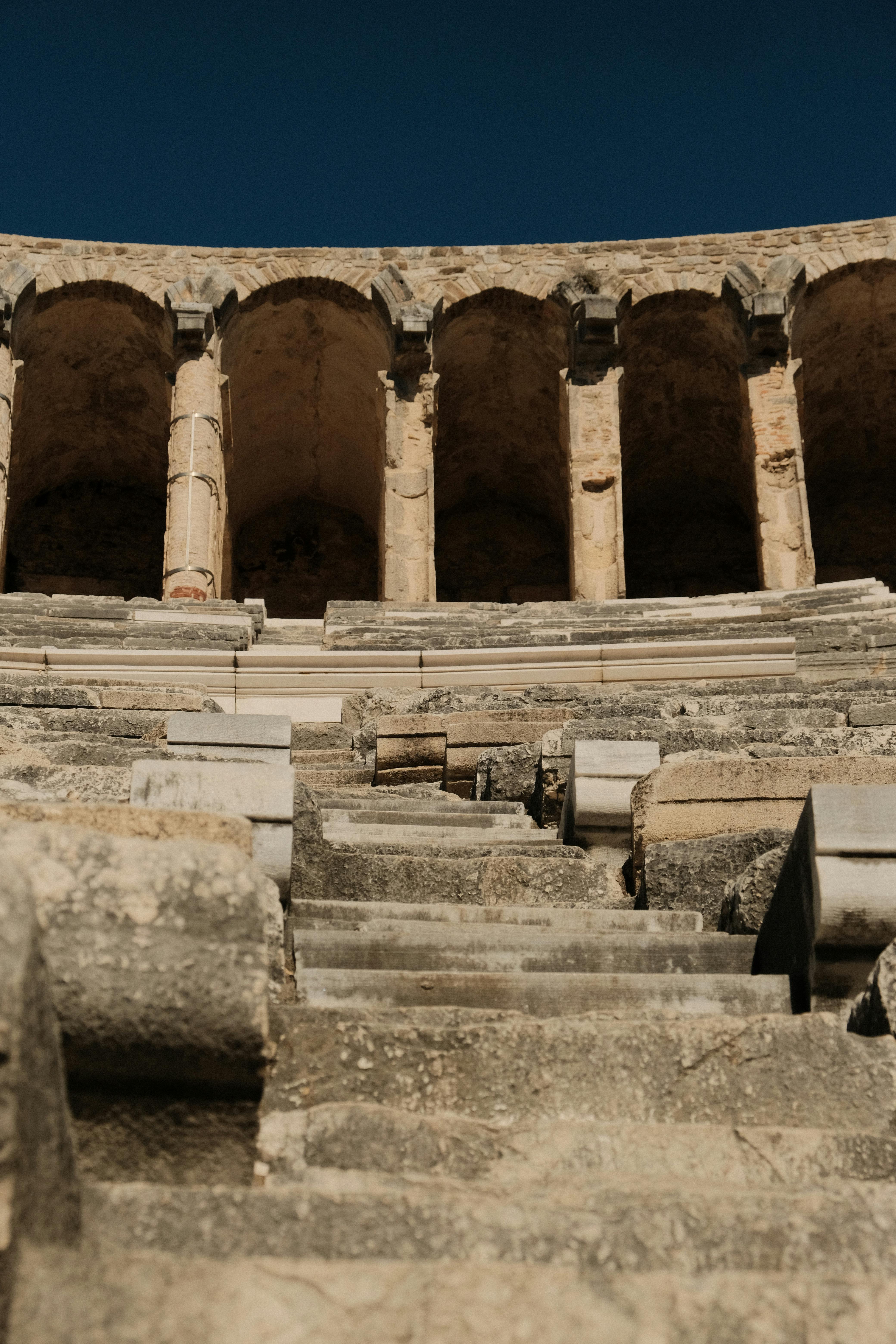 Ücretsiz Masmavi bir gökyüzünün altında, yıpranmış taş kemerleri ve basamaklarıyla tarihi bir Roma amfitiyatrosu. Stok Fotoğraflar