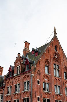 Brick building facade in Bruges showcasing Gothic Revival architecture against a cloudy sky.