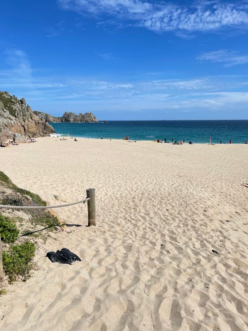 Free A serene view of Porthcurno Beach with golden sands and a vibrant blue sky. Stock Photo