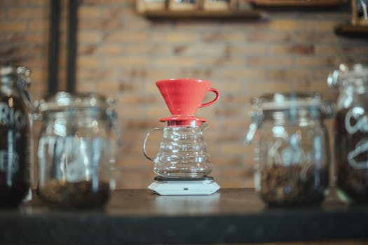 A red coffee dripper on a scale, surrounded by jars, showcased in a brick-walled cafe.