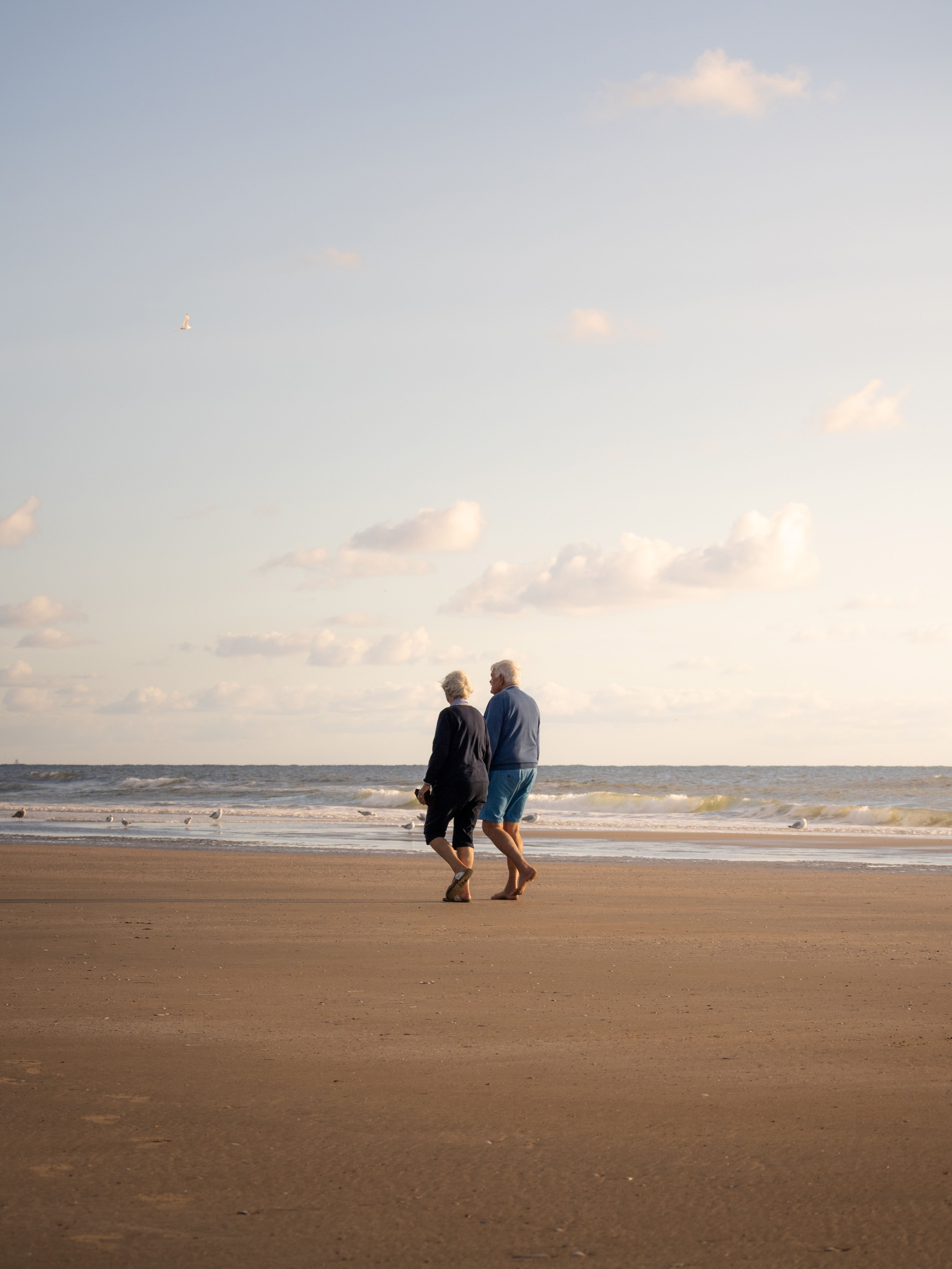 Een sereen moment van een ouder echtpaar dat langs het strand van IJmuiden wandelt onder een pastelkleurige hemel.