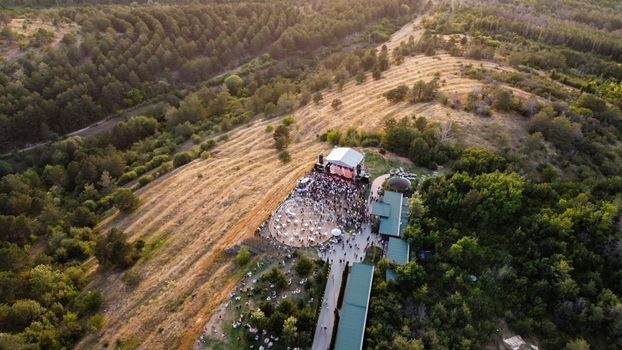 A scenic aerial shot capturing a lively outdoor music festival surrounded by lush greenery in Kotayk Province, Armenia.