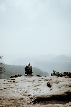 Lone traveler gazing at misty valley from rocky cliff in Bad Schandau, Germany, capturing serene outdoors.