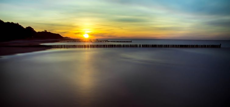 Serene ocean view at sunset with reflective water and silhouetted wooden jetties.