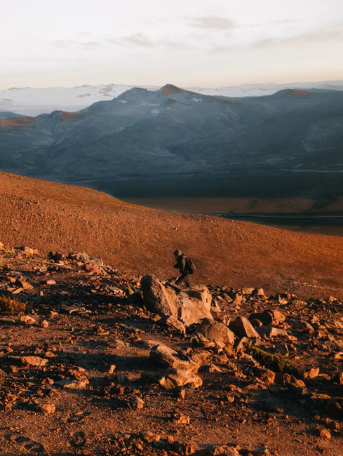 A lone hiker explores the rocky terrain of the Andes during a breathtaking sunrise.