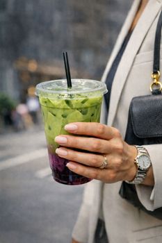 A stylish person holding a green matcha and berry layered drink in an urban setting.