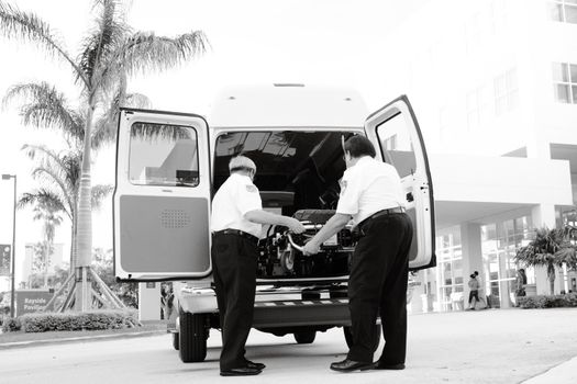Black and white photo of emergency responders loading equipment into an ambulance outside a medical building.