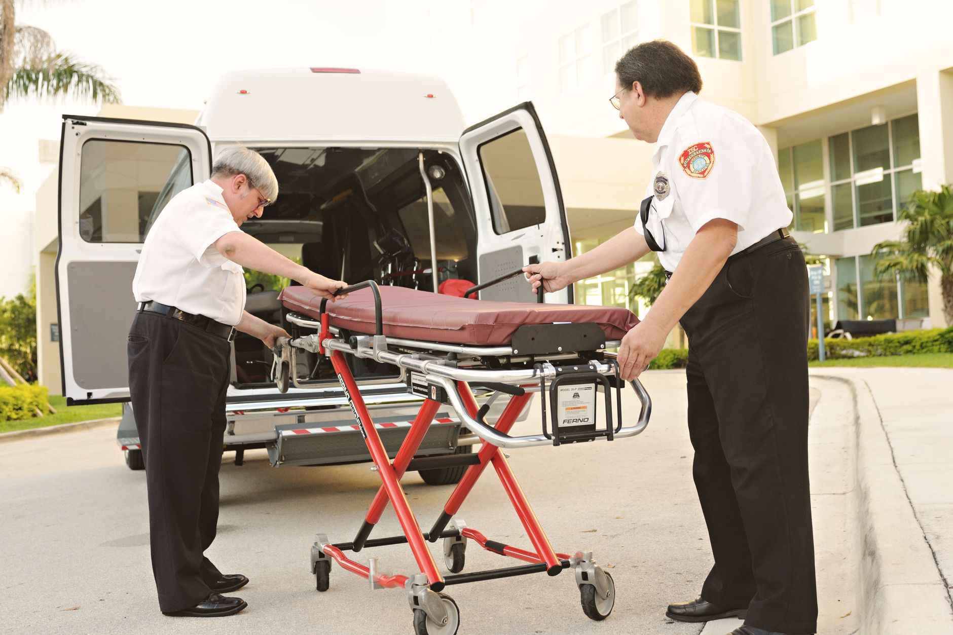 Two EMTs handle a stretcher outside a building, readying for patient transport.