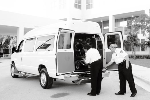 Paramedics load a stretcher into an ambulance van outside a hospital building.
