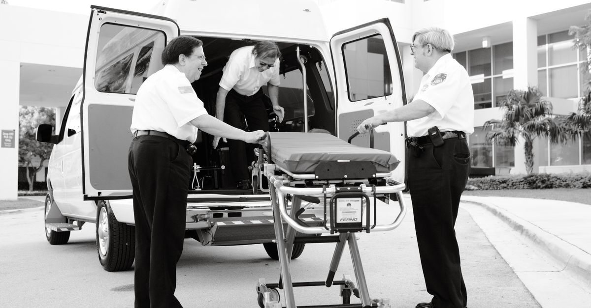 Monochrome image of paramedics loading a stretcher into an ambulance outside a hospital.
