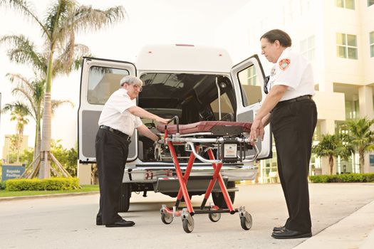 Two emergency responders load a stretcher into an ambulance outdoors, depicting medical assistance.