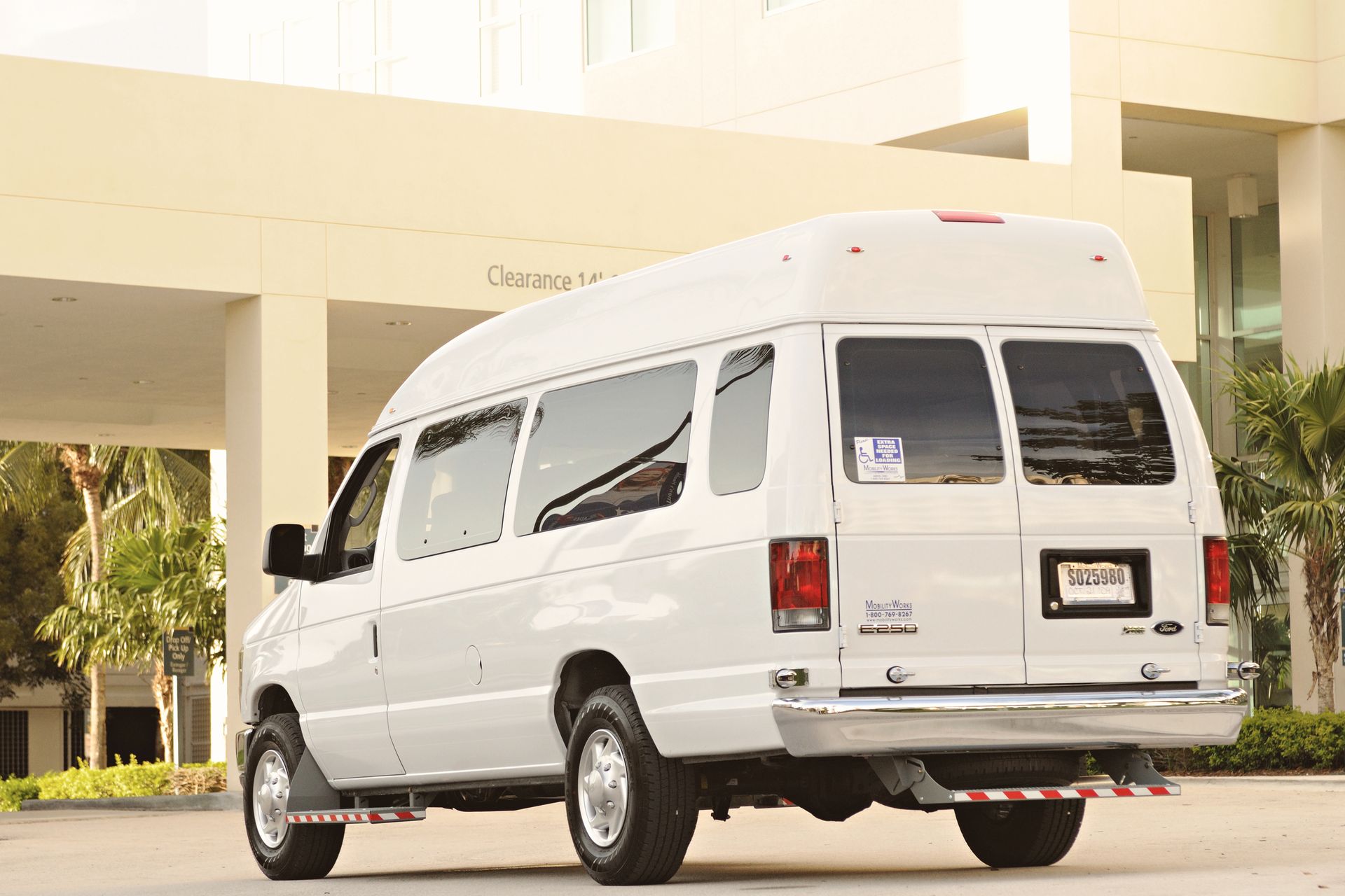 White passenger van parked outside a modern building with palm trees — airport shuttle transfer