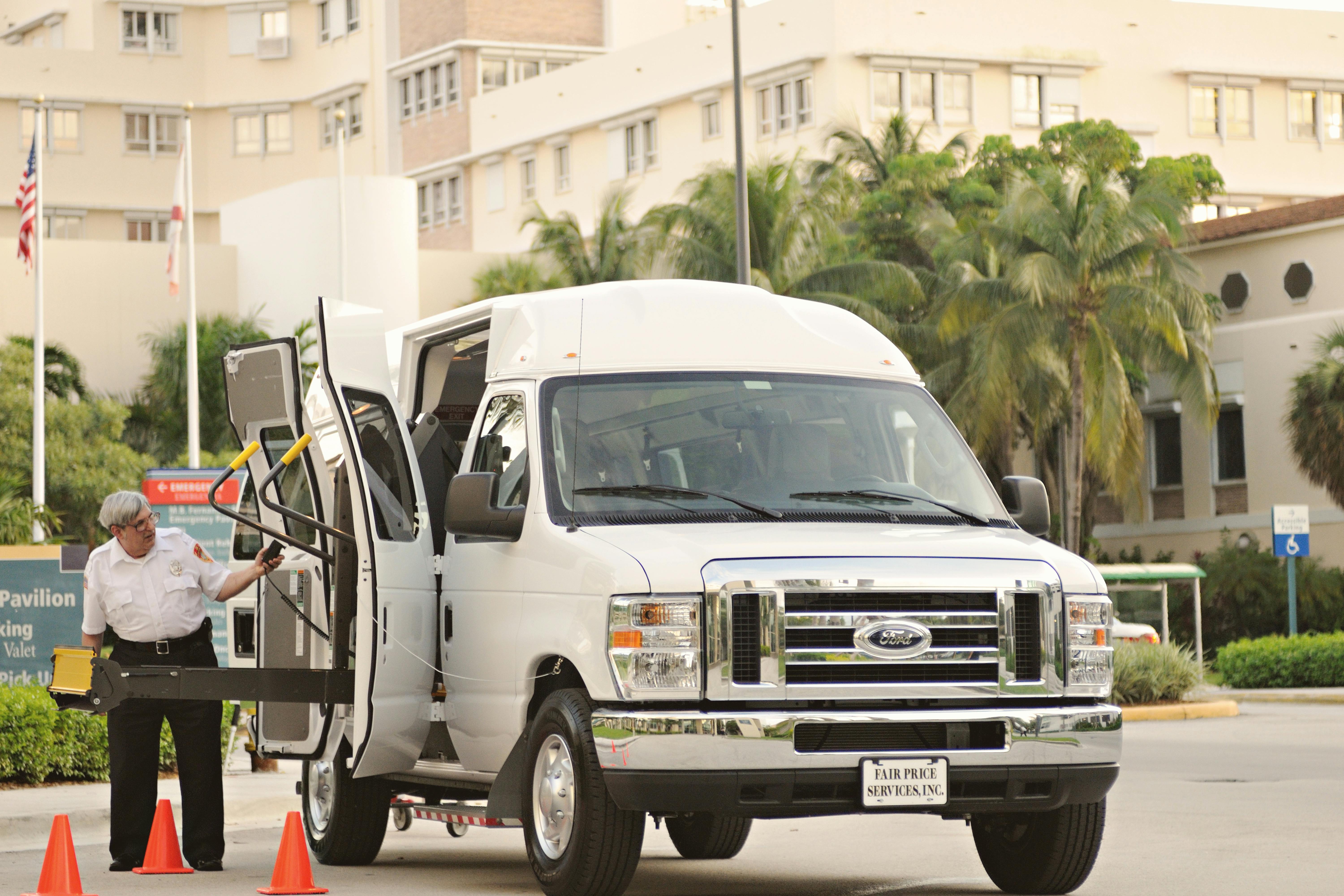 Van with wheelchair lift and driver assisting, located outdoors near a hospital or medical facility.